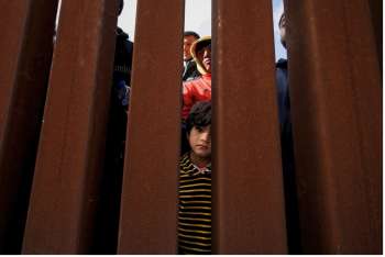 A young boy peers through the border wall as migrants gather between primary and secondary border fences in San Diego as the United States prepares to lift COVID-19-era restrictions known as Title 42, that have blocked migrants at the U.S.- Mexico border from seeking asylum since 2020, near San Diego on May 8, 2023. Photo by Mike Blake, Reuters